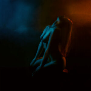 Color fine art nude photography of a kneeling female figure illuminated by blue and amber light